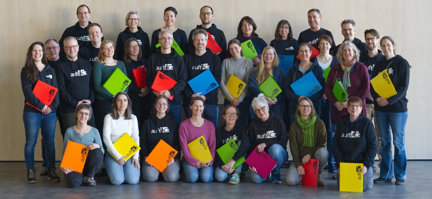 Gruppenfoto des Chors auftACt: Sängerinnen und Sänger in schwarzen Pullovern mit bunten Notenmappen in Rot, Grün, Orange, Blau, Gelb und Pink